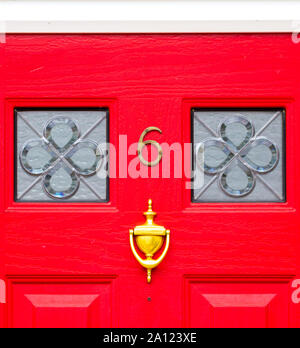 Haus Nummer 6 auf eine helle rote hölzerne Eingangstür mit Glasscheiben und Türklopfer Stockfoto