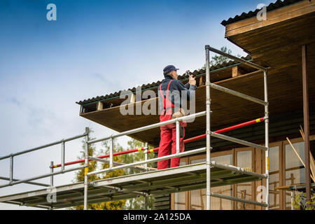 Mann, auf Gerüsten und alten Holzhaus Dachkonstruktion wiederherstellen Stockfoto