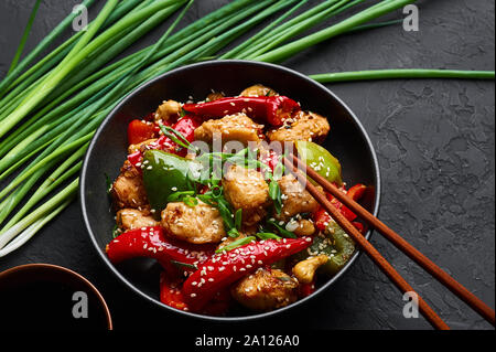 Schezwan Huhn oder Dragon Huhn in schwarz Schüssel am dunklen Schiefer Hintergrund. Szechuan Chicken ist beliebt indo-chinesischen würzigen Gericht mit Paprika, ch Stockfoto