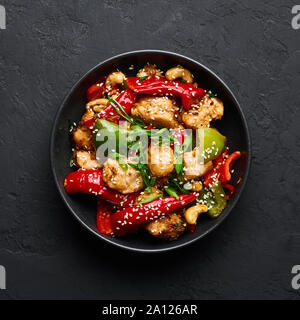 Schezwan Huhn oder Dragon Huhn in schwarz Schüssel am dunklen Schiefer Hintergrund. Szechuan Chicken ist beliebt indo-chinesischen würzigen Gericht mit Paprika, ch Stockfoto