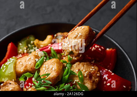 Schezwan Huhn oder Dragon Huhn in schwarz Schüssel am dunklen Schiefer Hintergrund. Szechuan Chicken ist beliebt indo-chinesischen würzigen Gericht mit Paprika, ch Stockfoto