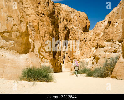 Beduinen in Weiß geht in der Schlucht in der Wüste zwischen den Felsen Stockfoto