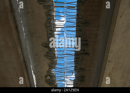 Unter der Brücke. Loch mit einem blauen Himmel. Abstrakte Konstruktion Hintergrund. Metallstangen in Beton. Alte Objekt unter Rekonstruktion. Stockfoto