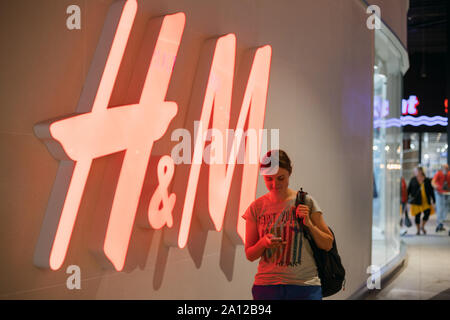 Tocksfors, Schweden - Juni 26, 2019: Junge Frau, die in der Nähe von Red Logo H&M Hennes & Mauritz Marke an der Store in der Shopping Mall Stockfoto