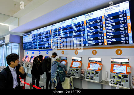 Tokio Haneda International Airport. Terminal 1 Interieur. Menschen mit einer Reihe von Bus Ticket Maschinen A und B, mit beleuchtetem Zeitplan vor. Stockfoto