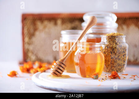 Kräuter Honig im Glas mit Pendelarm, Honig, Biene Blütenstaub Granulat, calendula Blüten auf grauem Hintergrund Stockfoto