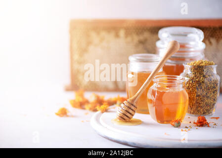 Kräuter Honig im Glas mit Pendelarm, Honig, Biene Blütenstaub Granulat, calendula Blüten auf grauem Hintergrund Stockfoto