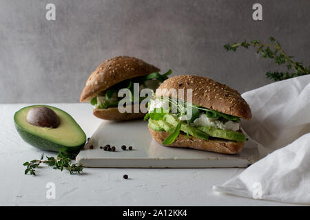 Zwei Sandwiches von Vollkorn Glutenfreie hausgemachtes Brot mit Avocado und Ricotta auf Weiß rustikal Keramik Schneidbrett. Gesunde hausgemachte Stockfoto