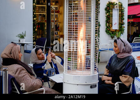 Drei muslimische Damen warten Weihnachten auf ihren Auftrag in einem Außenrestaurant, St. Christopher's Place, High-End-Einkaufsstraße in Central London Stockfoto