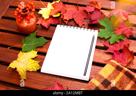 Leer Notebook öffnen Sie mit einem Bleistift auf einem Holztisch mit Herbst Ahorn Blätter verstreut herum und eine Vase mit Rowan. Stockfoto