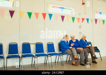 Drei ältere Frauen sprechen und saß im Innenbereich auf blauen Stühlen in einer Halle mit wimpelketten dekoriert. Stockfoto