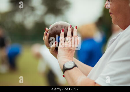 Eine Nahaufnahme von einer älteren Frau mit einem Boccia, bereit, ihren Schoß zu nehmen. Sie trägt Nagellack und eine Uhr. Stockfoto