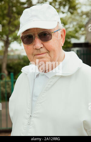 Ein Portrait eines älteren Mannes an einem bowling green lächelnd. Er trägt eine Sonnenbrille. Stockfoto