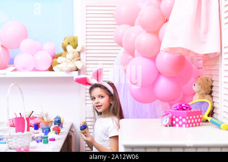 Die Werte der Familie, Kindheit, Kunst Tochter malen handgefertigte Ei bei Party Luftballons. Frohe Ostern mit kleinen Mädchen malen Eier. Ostern, Kind in rosa Häschen Ohr Stockfoto