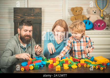 Familie spiele Konzept. Eltern mit glücklichen Gesichtern und Kid macht brick Konstruktionen. Vater, Mutter und Sohn im Spielzimmer auf hellen Hintergrund. Junge Stockfoto