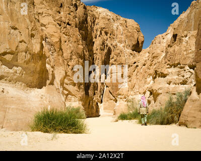 Beduinen in Weiß geht in der Schlucht in der Wüste zwischen den Felsen Stockfoto