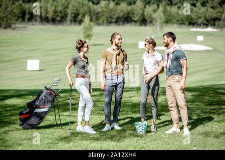 Junge und elegante Freunde zusammen mit Golfausrüstung, Spaß beim Golf spielen auf den schönen Kurs an einem sonnigen Tag Stockfoto