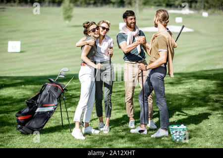 Junge elegante Freunde treffen auf dem Golfplatz vor dem Spiel, Spaß zusammen an einem sonnigen Tag Stockfoto