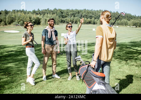 Junge elegante Freunde treffen auf dem Golfplatz vor dem Spiel, Spaß zusammen an einem sonnigen Tag Stockfoto