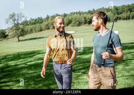 Zwei männliche beste Freunde gehen mit Golfausrüstung auf schönen spielen, reden und Spaß haben während eines Spiels an einem sonnigen Tag Stockfoto