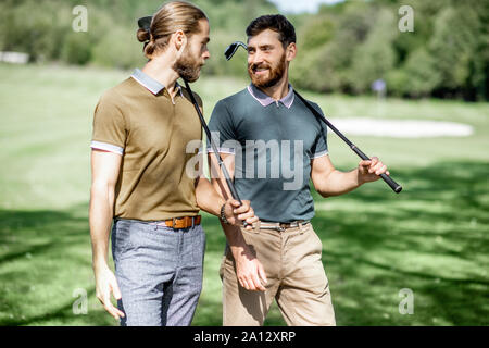 Zwei männliche beste Freunde gehen mit Golfausrüstung auf schönen spielen, reden und Spaß haben während eines Spiels an einem sonnigen Tag Stockfoto