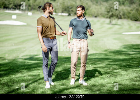 Zwei männliche beste Freunde gehen mit Golfausrüstung auf schönen spielen, reden und Spaß haben während eines Spiels an einem sonnigen Tag Stockfoto