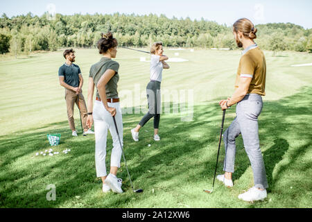 Gruppe von einem jungen Menschen lässig gekleidet, Golf spielen auf dem Golfplatz an einem sonnigen Tag, Frau Schwingen einen Putter Stockfoto