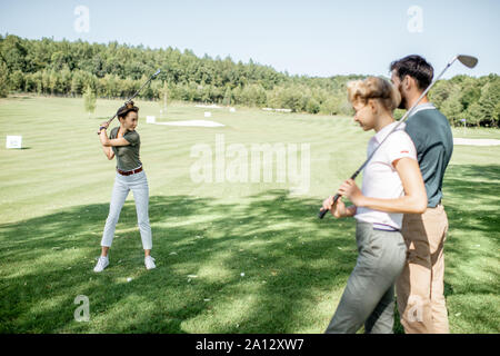 Gruppe von einem jungen Menschen lässig gekleidet, Golf spielen auf dem Golfplatz an einem sonnigen Tag, Frau Schwingen einen Putter Stockfoto