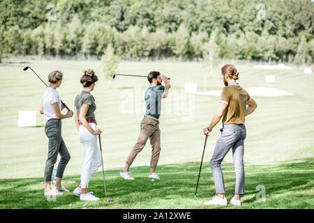 Gruppe von einem jungen Menschen lässig gekleidet, Golf spielen auf dem Golfplatz an einem sonnigen Tag, man Schwingen einen Putter Stockfoto