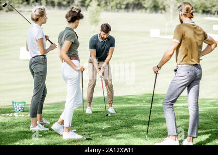 Gruppe von einem jungen Menschen lässig gekleidet, Golf spielen auf dem Golfplatz an einem sonnigen Tag, man Schwingen einen Putter Stockfoto