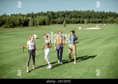 Gruppe von Freunden reden und gehen mit Putter beim Golf spielen auf den schönen Kurs an einem sonnigen Tag Stockfoto