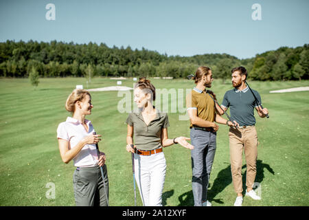 Gruppe von Freunden reden und gehen mit Putter beim Golf spielen auf den schönen Kurs an einem sonnigen Tag Stockfoto