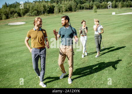 Gruppe von Freunden reden und gehen mit Putter beim Golf spielen auf den schönen Kurs an einem sonnigen Tag Stockfoto