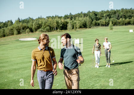 Gruppe von Freunden reden und gehen mit Putter beim Golf spielen auf den schönen Kurs an einem sonnigen Tag Stockfoto
