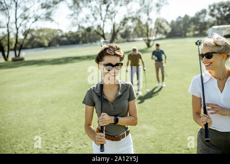 Zwei weibliche beste Freunde zusammen zu Fuß mit dem Spielen der Putter während ein Golfspiel auf einem Kurs, der an einem sonnigen Tag Stockfoto