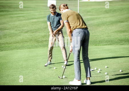 Zwei Männer spielen Golf, schoss den Ball mit dem Putter in die Bohrung auf dem Kurs, der an einem sonnigen Tag Stockfoto