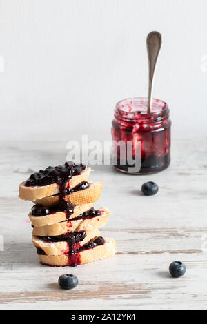 Ein Haufen von Brot mit Blaubeer-marmelade verschmiert. Nächste jam in einem Glas zu Blueberry. Ein helles Holz- Tabelle. Stockfoto