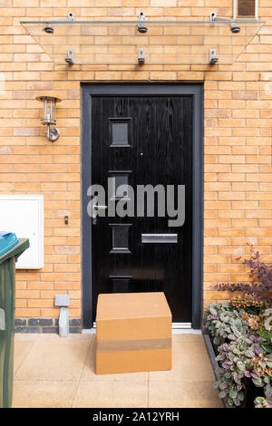 Ein großes Paket steht vor einer geschlossenen Tür, eine typisch englische Red brick House. Stockfoto