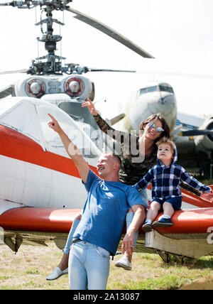 Mutter, Vater und Kind aufgeregt Sitzen im Flugzeug Flügel in Aviation Museum. Happy Family suchen auf Sky auf Exkursion, Hubschrauber oder Flugzeug auf Hintergrund, s Stockfoto