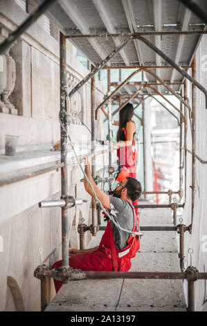 Zwei Arbeiter auf Gerüst, die Arbeit an der Restaurierung der Fassade des alten Gebäudes durchführen. Reparieren und Renovieren Stockfoto