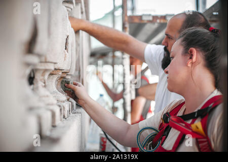 Zwei Arbeiter auf Gerüst, die Arbeit an der Restaurierung der Fassade des alten Gebäudes durchführen. Reparieren und Renovieren Stockfoto