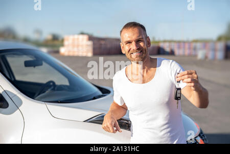 Eine männliche Fahrer steht in der Nähe ein Auto mit einem Schlüssel in der Hand und lächelt. Stockfoto