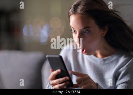 Erstaunt Frau Kontrolle smarrt Telefon Verbindung Geschwindigkeit sitzen auf einer Couch in der Nacht zu Hause Stockfoto