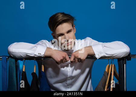 Unternehmer im weißen Hemd auf blauem Hintergrund. Bekleidung, Dressing, Schrank. Man Hände auf Rack mit Kleidung im Schrank. Business Fashion, Style con Stockfoto