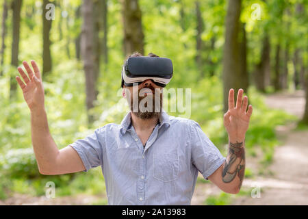 Bärtiger Mann mit 360 Grad Perspektive im VR-Brille. Aufgeregt Mann mit Bart tragen moderne Gerät das Roaming in Wäldern. Bärtige Hipster mit VR-hea Stockfoto