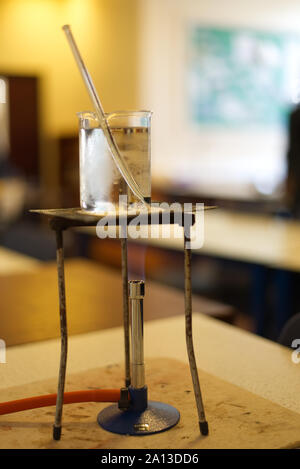 Heizung Wasser in ein Becherglas mit einem Gasbrenner in einer Schule Science Lab. Labor mit Studenten aus der Fokus in den Hintergrund. Praktische Untersuchung Stockfoto