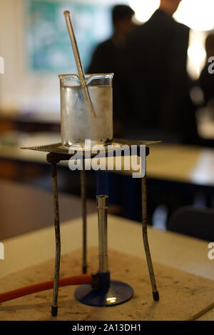 Heizung Wasser in ein Becherglas mit einem Gasbrenner in einer Schule Science Lab. Labor mit Studenten aus der Fokus in den Hintergrund. Praktische Untersuchung Stockfoto