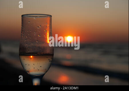 Glas Wein auf Sunrise, Sunset Hintergrund, auf dem Meer Stockfoto