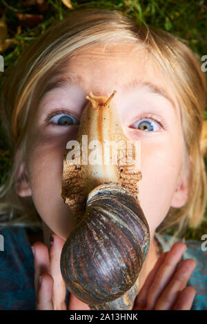 Porträt von präteen liebenswert Kind Mädchen spielt mit ihrem Haustier Riese afrikanische Schnecke (Achatina fulica). Schnecke krabbelt über das Gesicht. Stockfoto