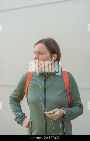 Brisk Walker weiblich Musik hören über Kopfhörer, Porträt der Frau in Sportkleidung in der städtischen Umgebung Stockfoto